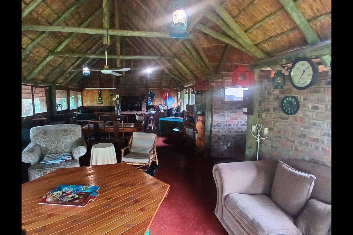 Spacious living area featuring a high vaulted thatched ceiling with exposed timber rafters, exposed brick walls, and durable concrete flooring.