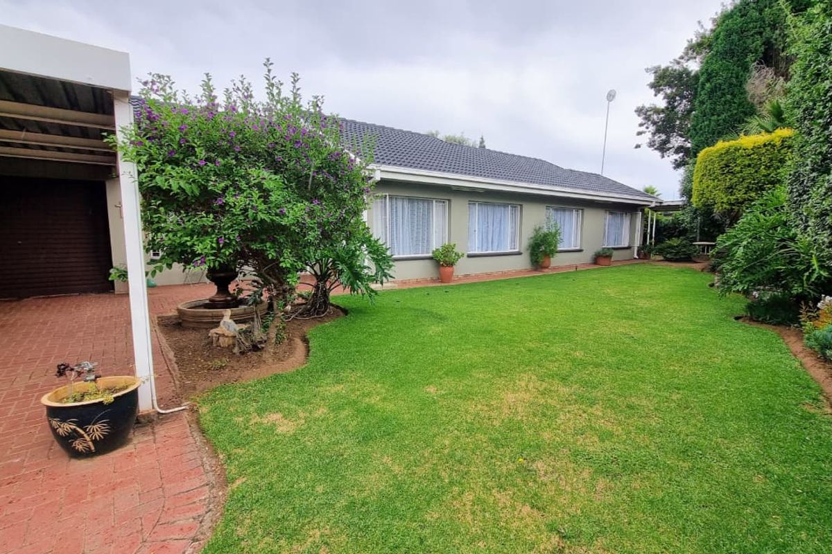 A well-maintained rear garden featuring a lush lawn, brick-paved area, and an attached carport, providing a pleasant outdoor space.