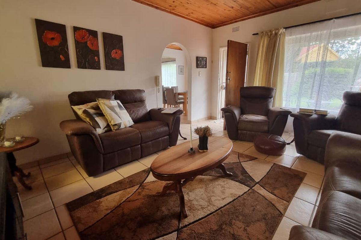 A comfortable living room featuring tiled flooring, a warm timber ceiling, and an arched entryway leading to the dining area.