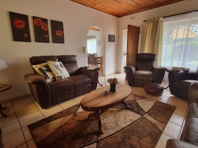 A comfortable living room featuring tiled flooring, a warm timber ceiling, and an arched entryway leading to the dining area.
