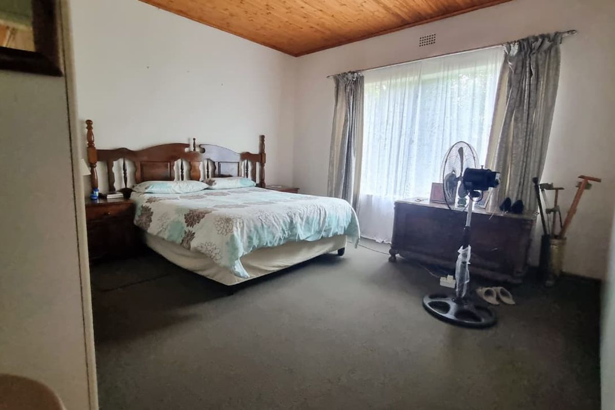 A spacious bedroom featuring a timber ceiling, built-in cupboards, and carpeted flooring, offering a functional layout with potential for modernization.