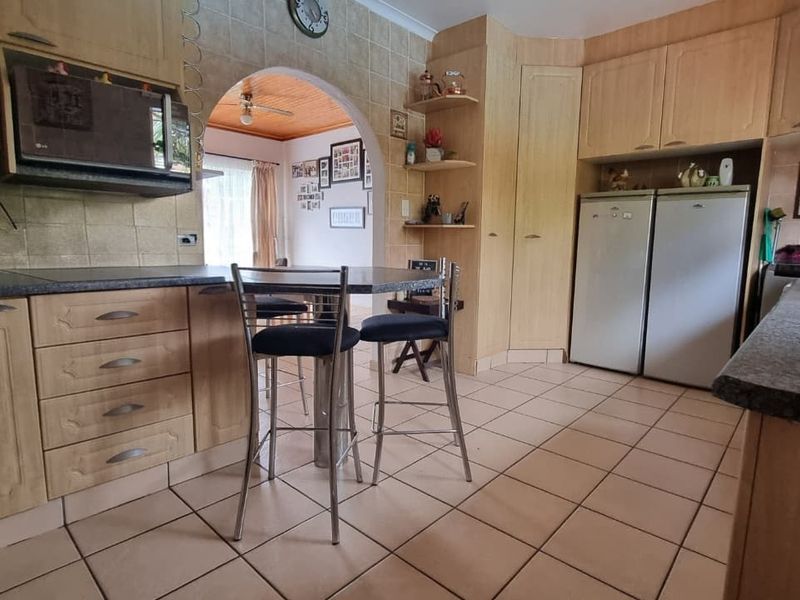 A functional kitchen featuring light wood cabinetry, tiled backsplash, and tiled flooring, with an arched opening leading to an adjacent living space.