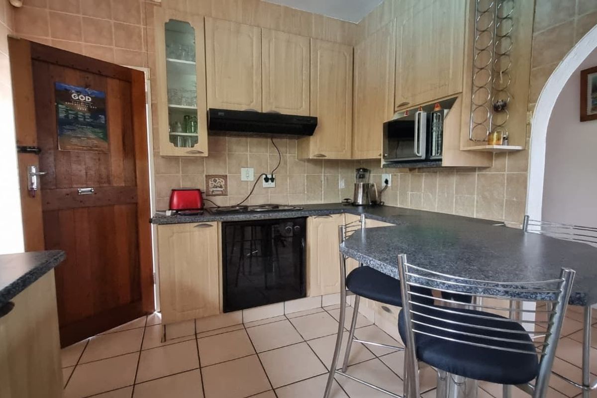A functional kitchen featuring light wood cabinetry, dark laminate countertops, tiled backsplash, and integrated appliances including an oven, hob, and microwave.