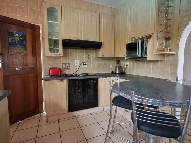 A functional kitchen featuring light wood cabinetry, dark laminate countertops, tiled backsplash, and integrated appliances including an oven, hob, and microwave.