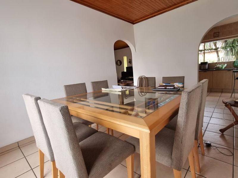 Open plan dining area featuring tiled flooring and timber ceiling, with arched access leading to a functional kitchen space.