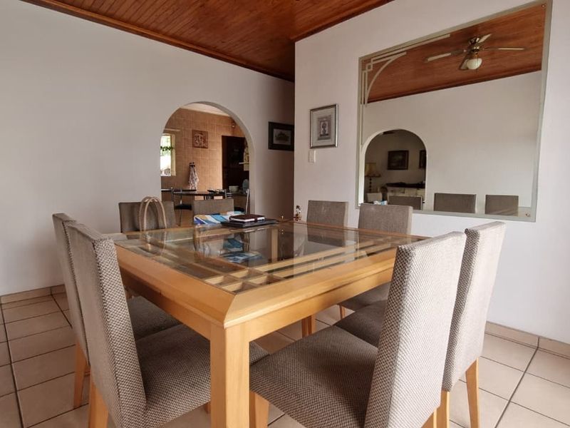 A dining room featuring a timber ceiling, tiled flooring, and an arched doorway leading to the kitchen area.