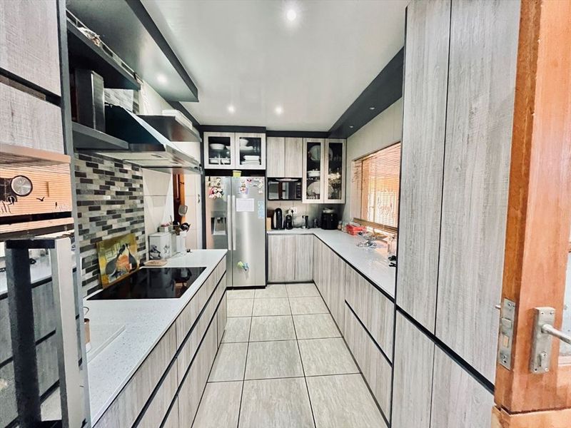 Modern galley-style kitchen featuring contemporary wood-grain cabinetry, stone countertops, integrated appliances, and sleek tiled flooring with recessed lighting.