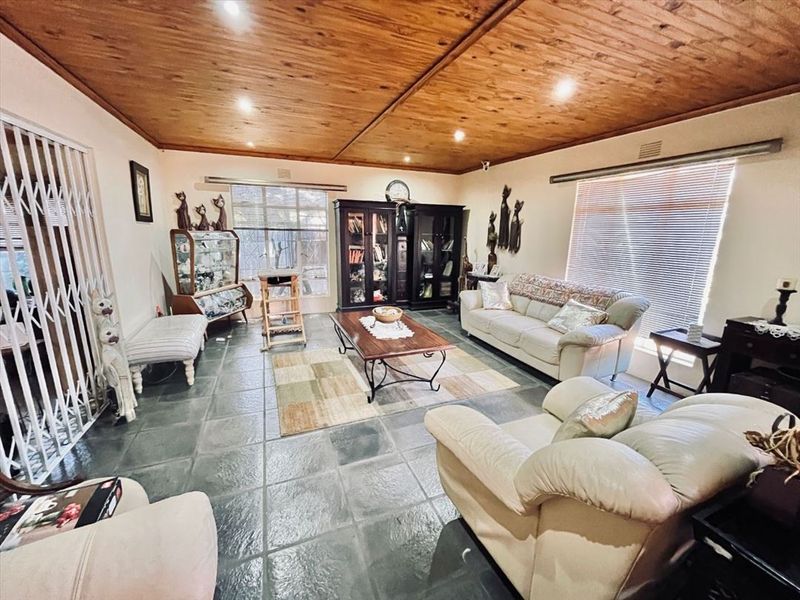 Spacious living room featuring a warm timber-clad ceiling, durable slate tile flooring, and large windows with venetian blinds for natural light.