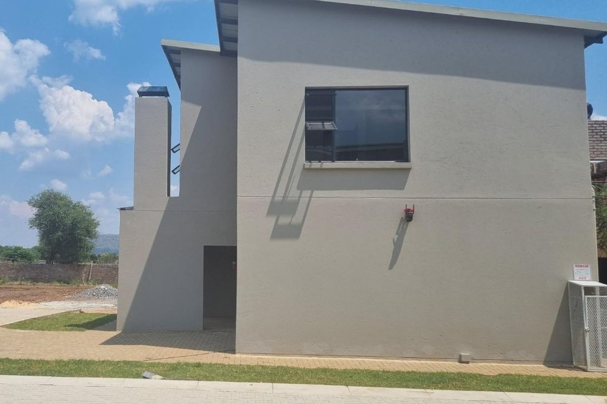 Rear view of the townhouse featuring a modern grey facade, external chimney, paved driveway, and secure utility enclosure.