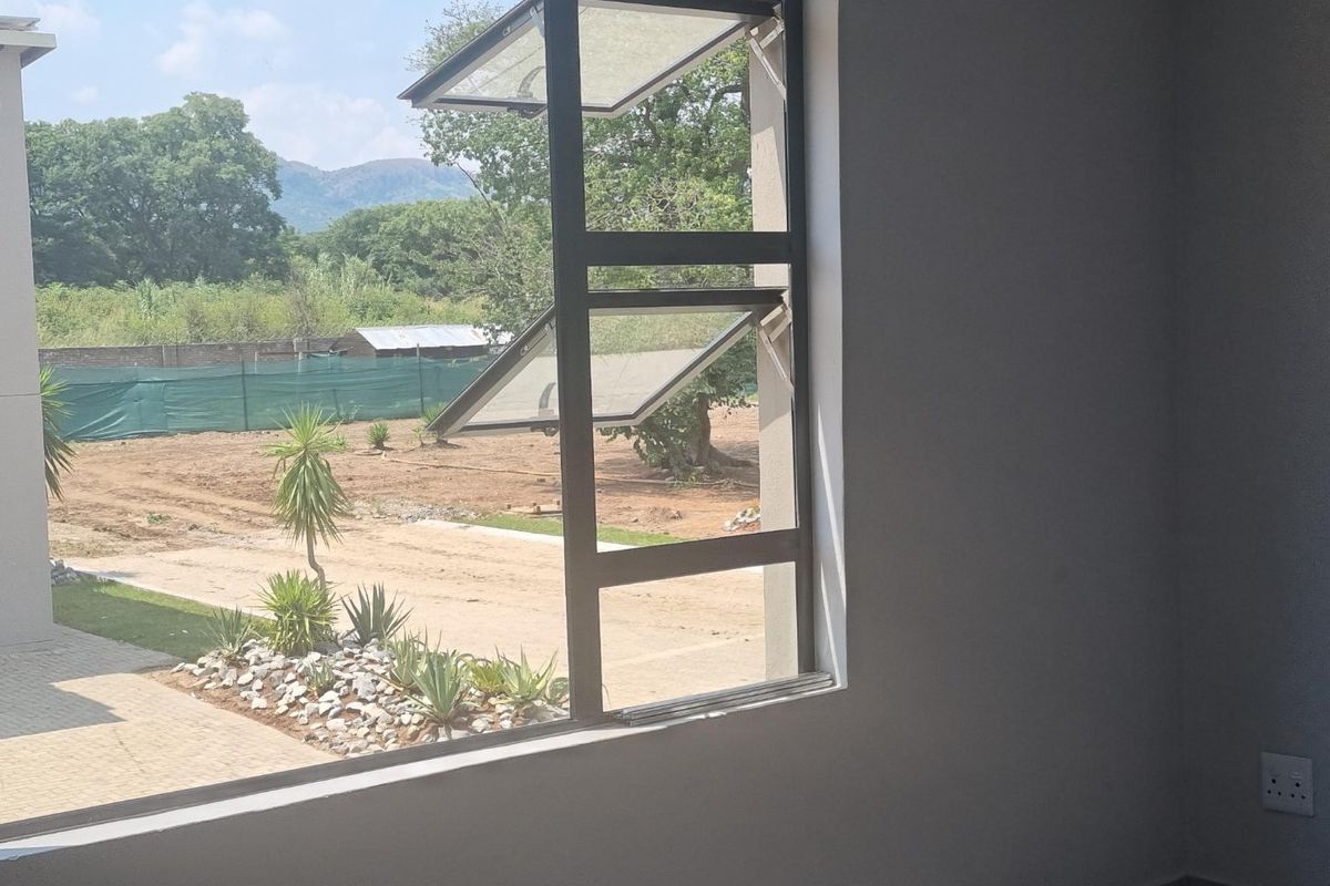 An interior view of an empty room featuring a modern aluminium casement window with a view of the surrounding landscape.