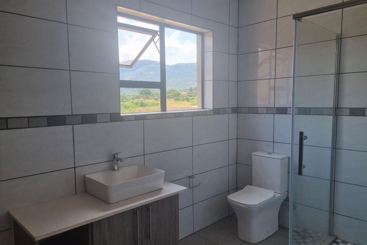 A modern bathroom featuring a vanity with a vessel sink, a toilet, and a glass-enclosed shower, finished with neutral wall and floor tiles.