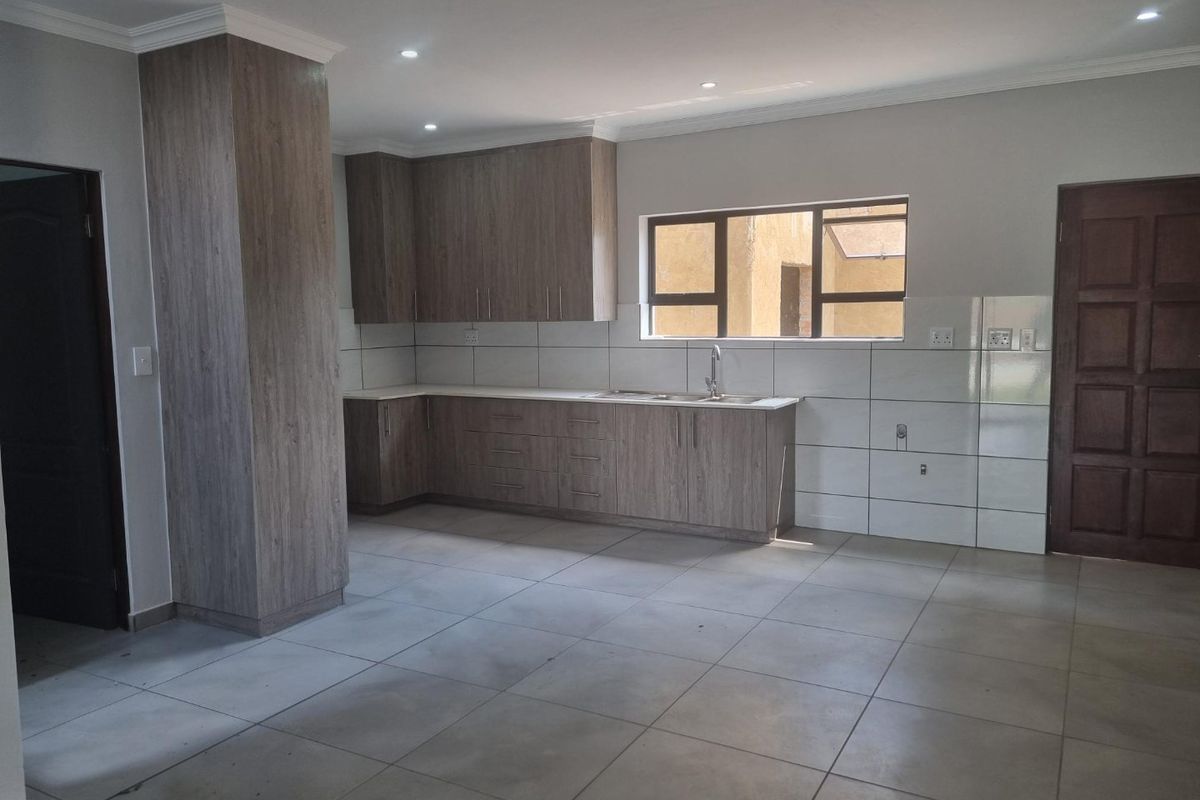 A clean, modern kitchen featuring wood-look cabinetry, tiled splashbacks, and a double sink, presented in an empty, well-maintained space.