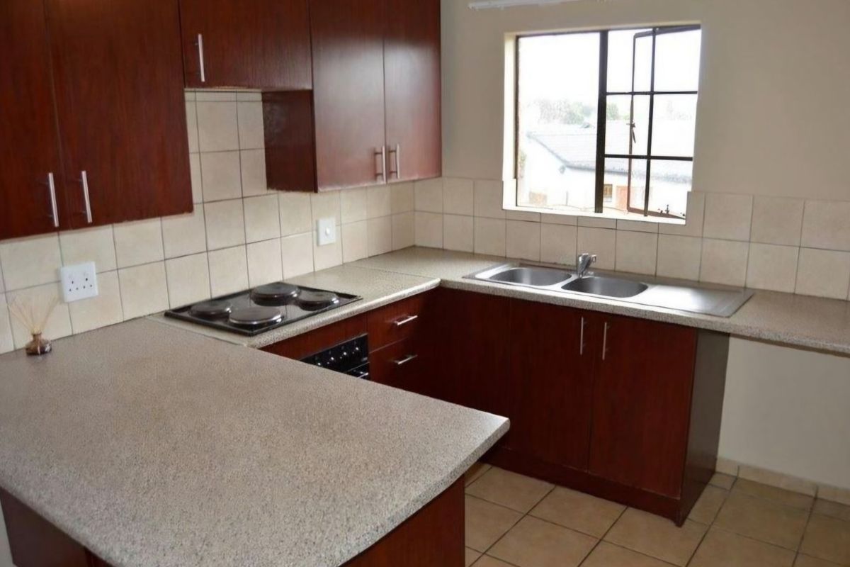 A functional kitchen featuring dark wood cabinetry, laminate countertops, a built-in electric hob and oven, and a double bowl stainless steel sink.