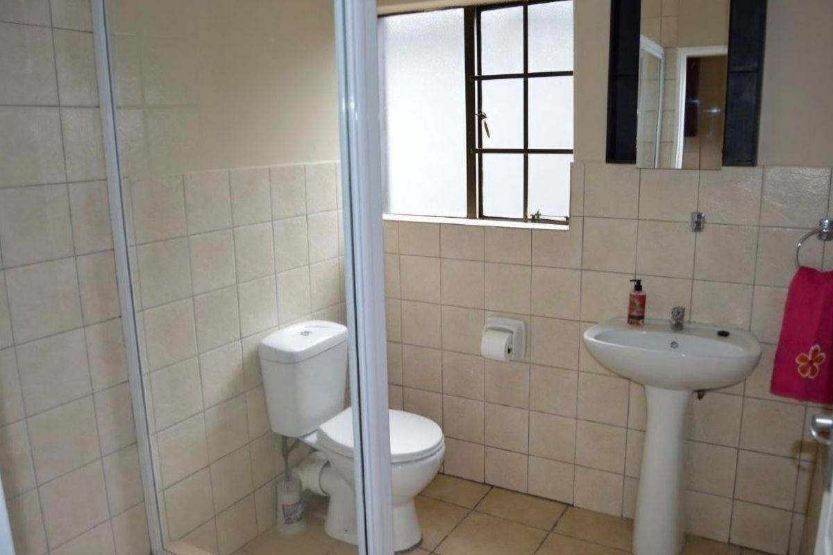 A functional bathroom featuring a pedestal basin, toilet, and a shower enclosure with tiled walls and flooring.