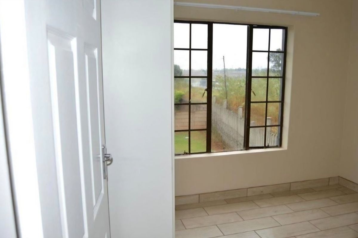A bright, empty bedroom featuring tiled flooring, a built-in cupboard, and a grid-pattern window overlooking the exterior.