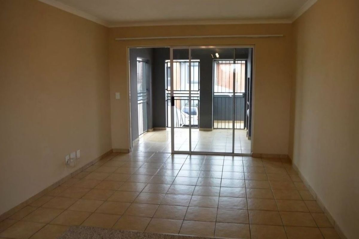 An empty living room featuring tiled flooring and a large sliding glass door leading to an outdoor patio area with security gates.