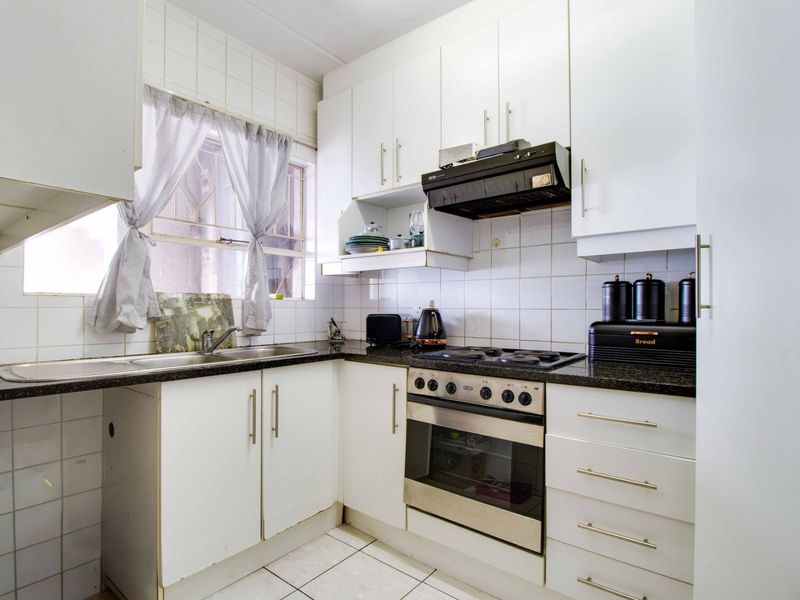 A functional kitchen featuring white built-in cabinetry, dark laminate countertops, a stainless steel sink, and integrated cooking appliances with tiled backsplash and flooring.
