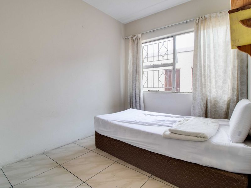 A simple bedroom featuring tiled flooring and a window fitted with security burglar bars.