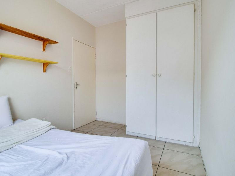 A functional bedroom featuring tiled flooring, a built-in wardrobe, and neutral wall finishes, offering a clean and simple living space.
