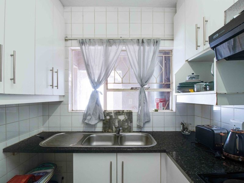 Compact kitchen featuring white cabinetry, granite countertops, a double bowl stainless steel sink, and a tiled backsplash with a window for natural light.