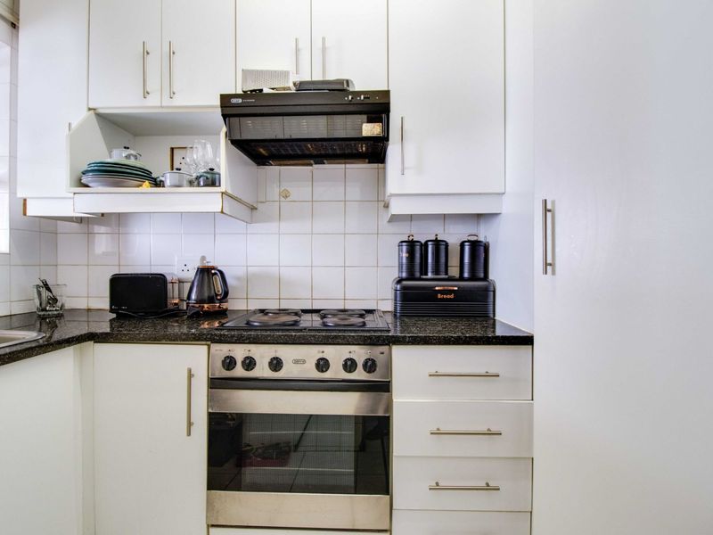 Compact kitchen featuring white cabinetry, granite countertops, a built-in oven with gas hob, and a tiled backsplash.