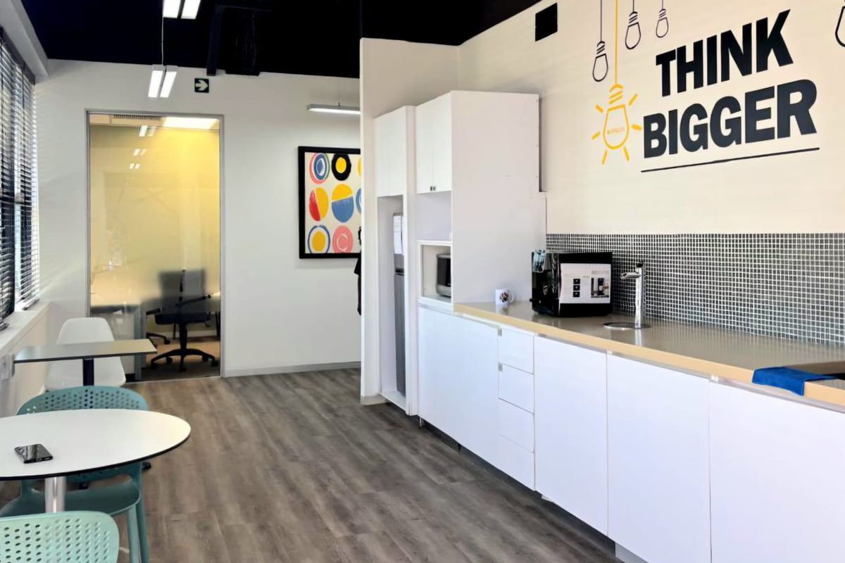 Modern commercial kitchenette featuring white cabinetry, mosaic tile backsplash, stainless steel countertop, and integrated sink, adjacent to a glass-partitioned office space.