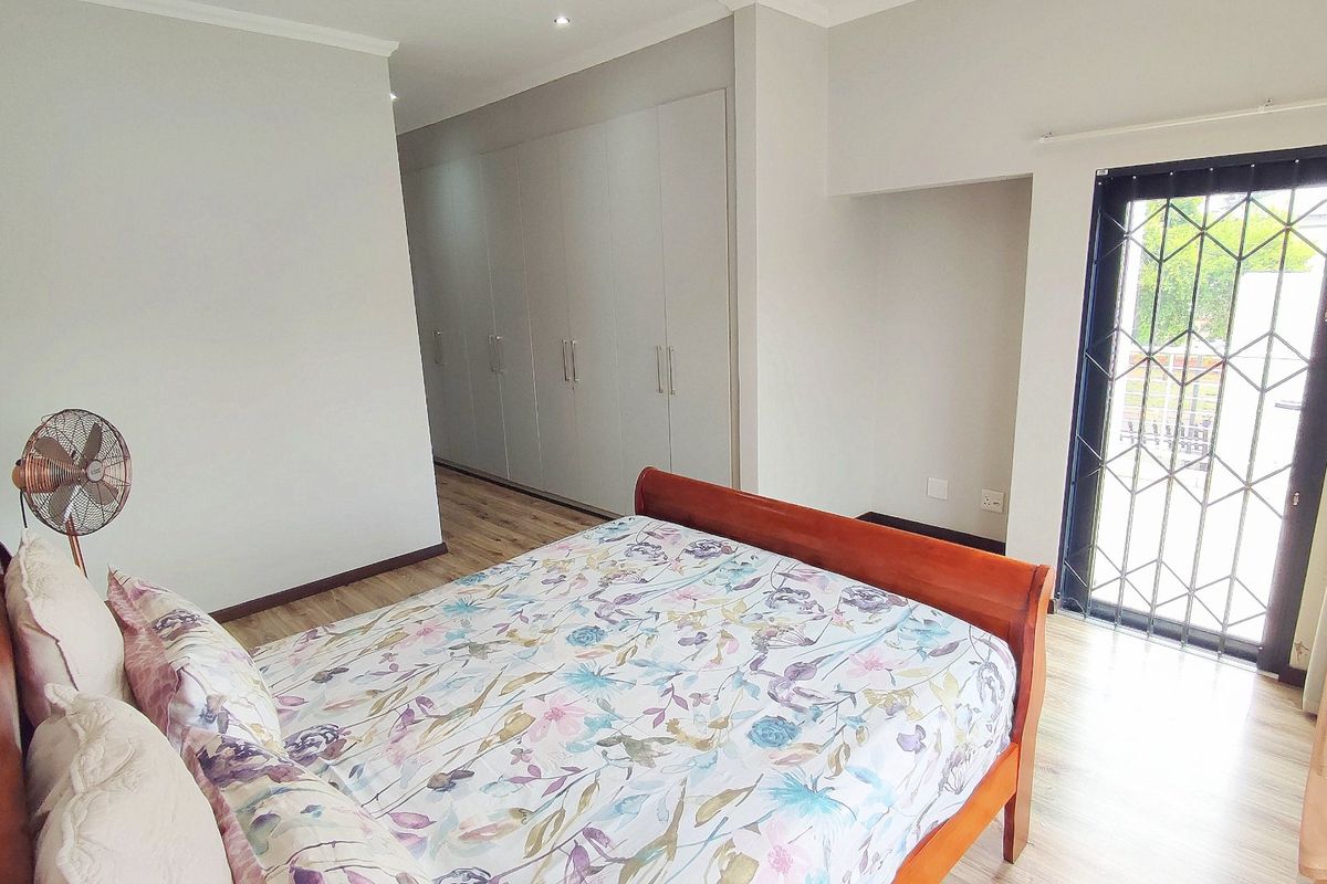 A well-maintained bedroom featuring light laminate flooring, extensive built-in cupboards, and a security gate leading to an outdoor area.