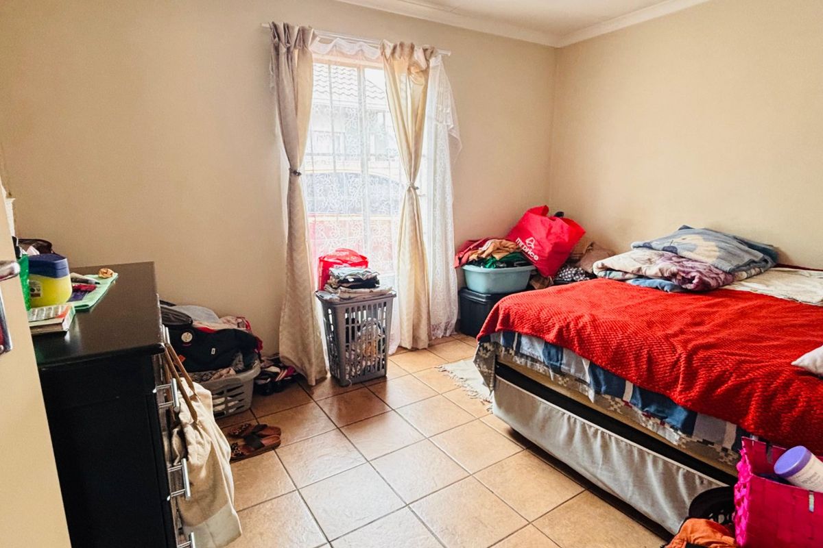 A bedroom featuring tiled flooring and a window with a security gate, providing natural light and access to the exterior.