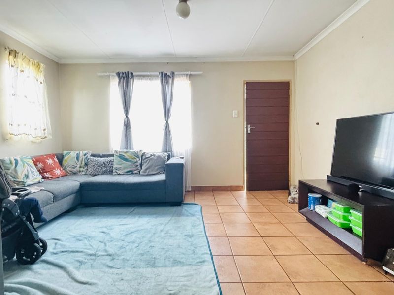 A functional living room featuring ceramic floor tiles, coved ceilings, and a solid core door, providing a neutral base for interior updates.