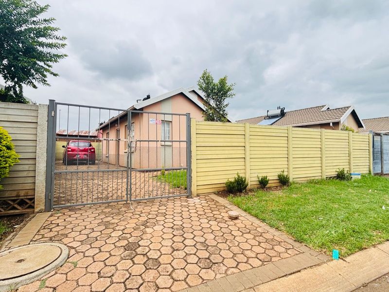 Front view of a residential property featuring a paved driveway, metal security gate, and precast boundary walling.