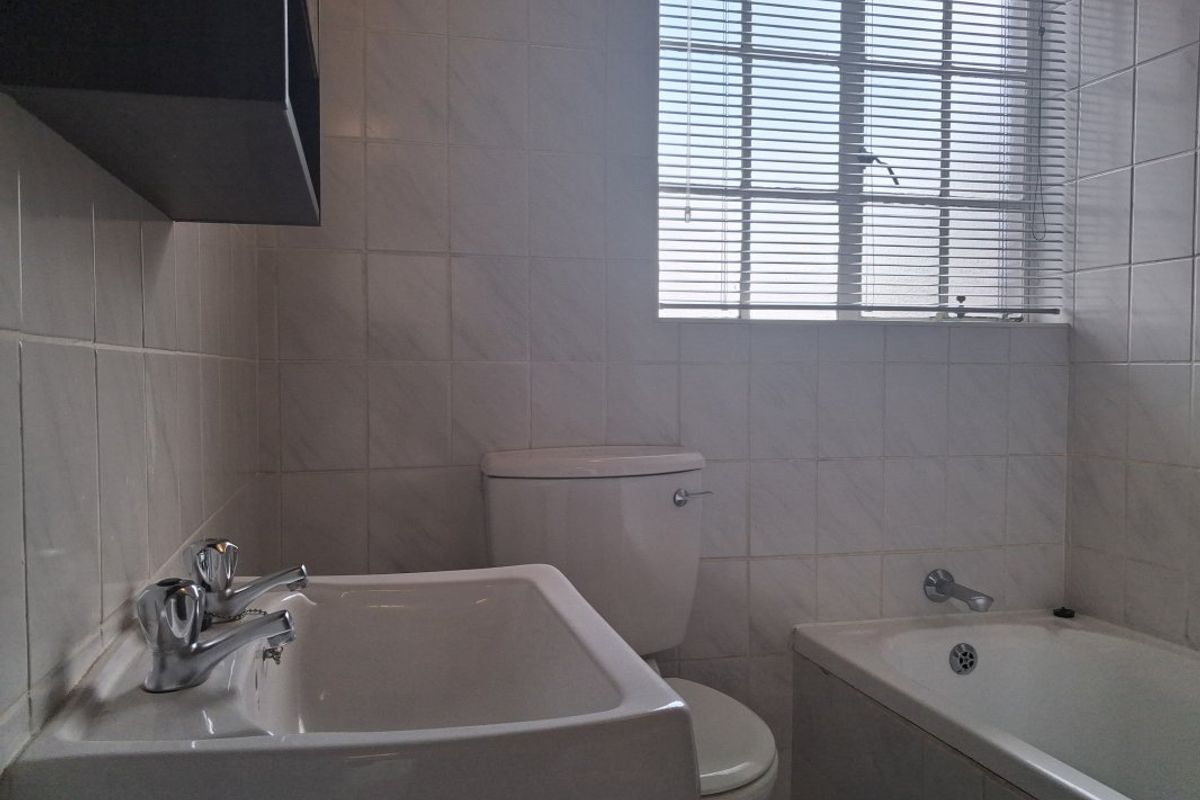 A functional bathroom featuring white wall tiles, a pedestal basin, a close-coupled toilet, and a built-in bathtub with a window.