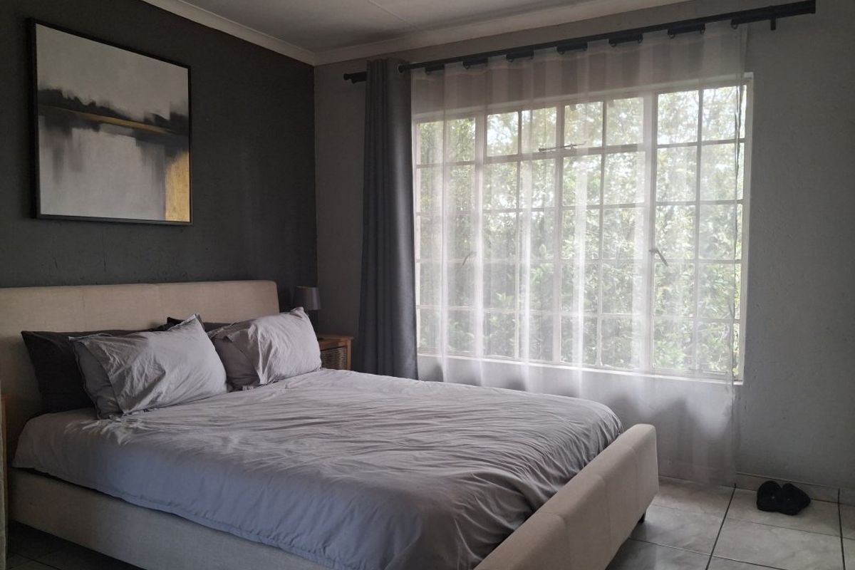A well-lit bedroom featuring tiled flooring, a large grid-pattern window, and a neutral color palette.