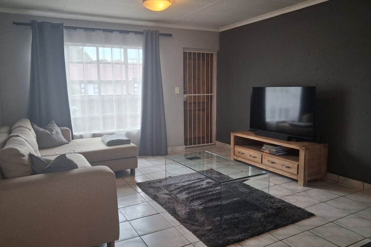 A living room featuring tiled flooring, a security gate, and a neutral color palette with a dark accent wall.