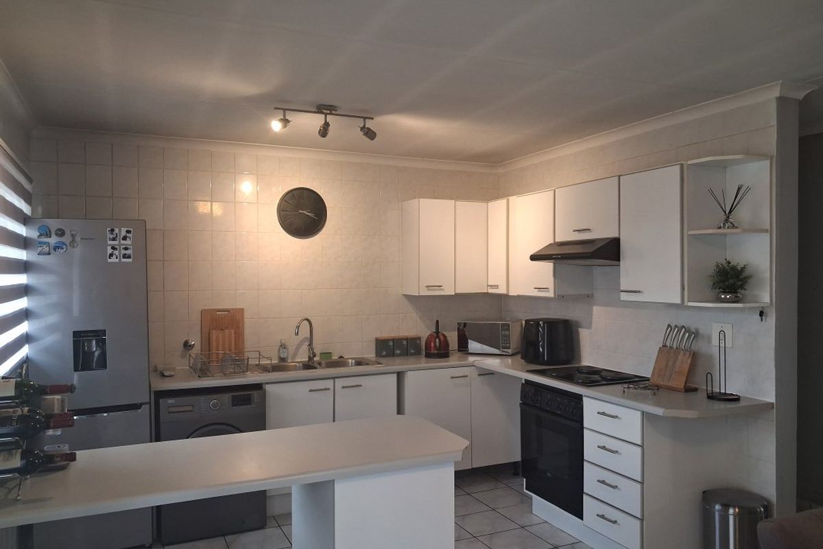 A functional kitchen featuring white cabinetry, tiled backsplash, built-in oven with hob, and a breakfast counter, providing a practical workspace.