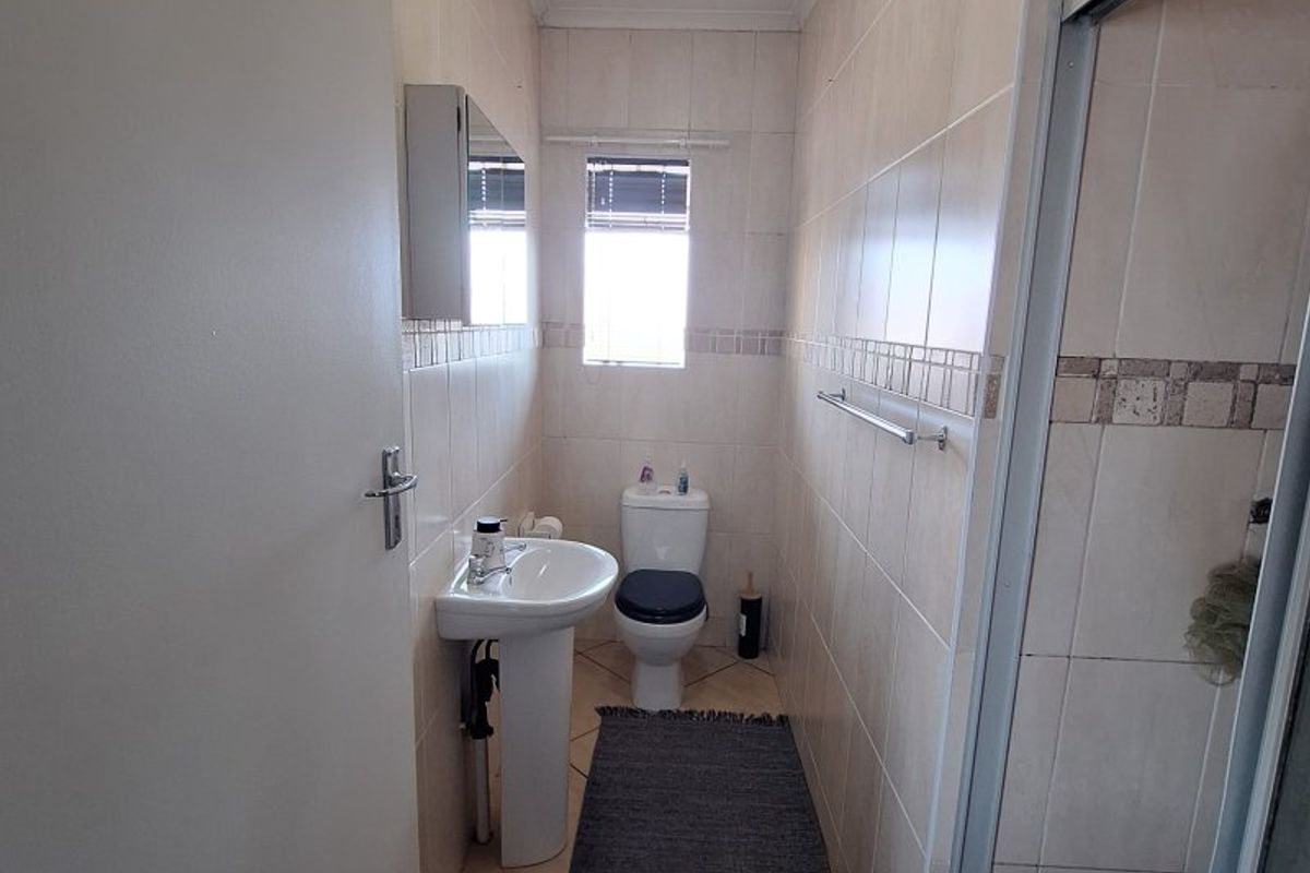 A functional bathroom featuring a pedestal basin, toilet, and a shower enclosure with tiled walls and flooring.