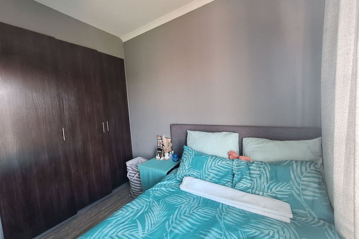 A well-maintained bedroom featuring dark wood built-in cupboards, laminate flooring, and neutral grey wall tones.