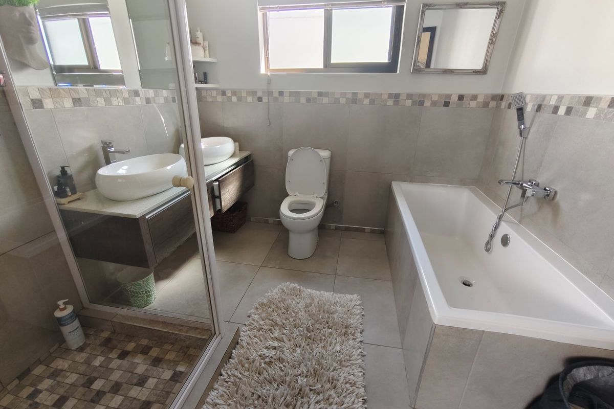 Modern bathroom featuring a double vanity with vessel sinks, a separate bathtub, and a glass-enclosed shower with neutral tiled finishes.