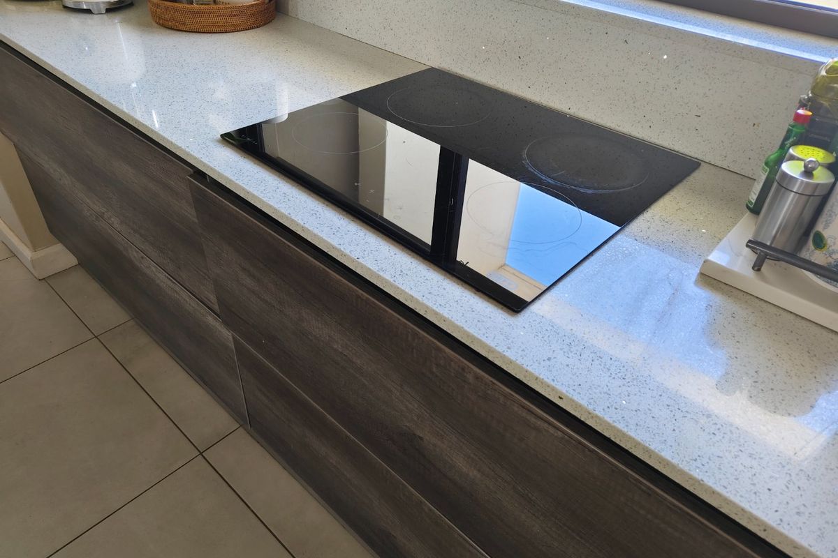 Modern kitchen featuring a sleek electric induction hob set into a high-quality quartz countertop with contemporary dark wood-grain cabinetry.