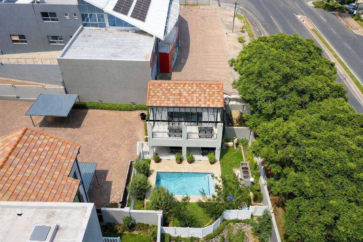 Aerial view of the property featuring a swimming pool, landscaped garden, paved driveway, carport, and a two-story building with a balcony and terracotta roof.