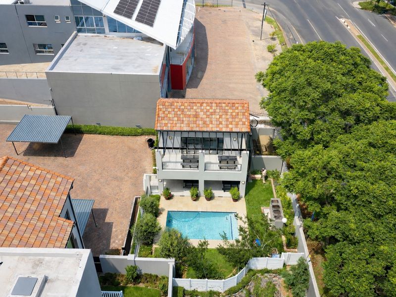Aerial view of the property featuring a swimming pool, landscaped garden, paved driveway, carport, and a two-story building with a balcony and terracotta roof.