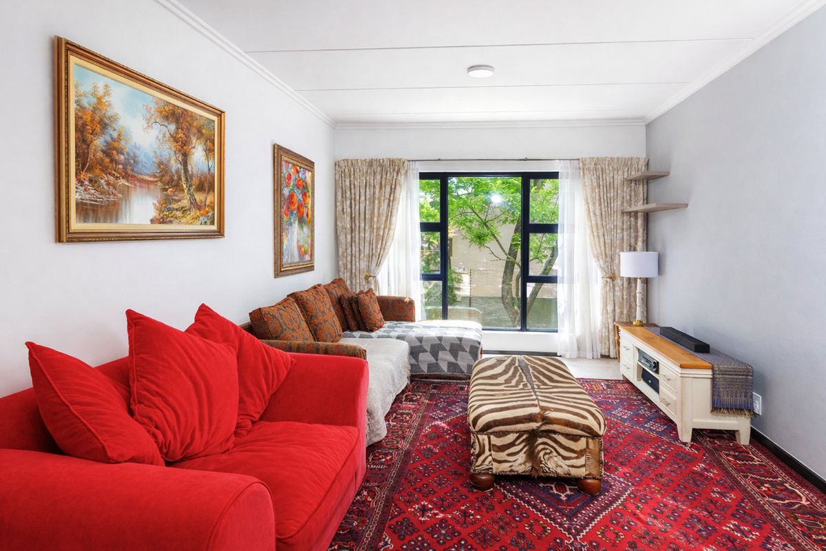 A well-lit living room featuring large windows with garden views, neutral wall finishes, and classic ceiling coving.