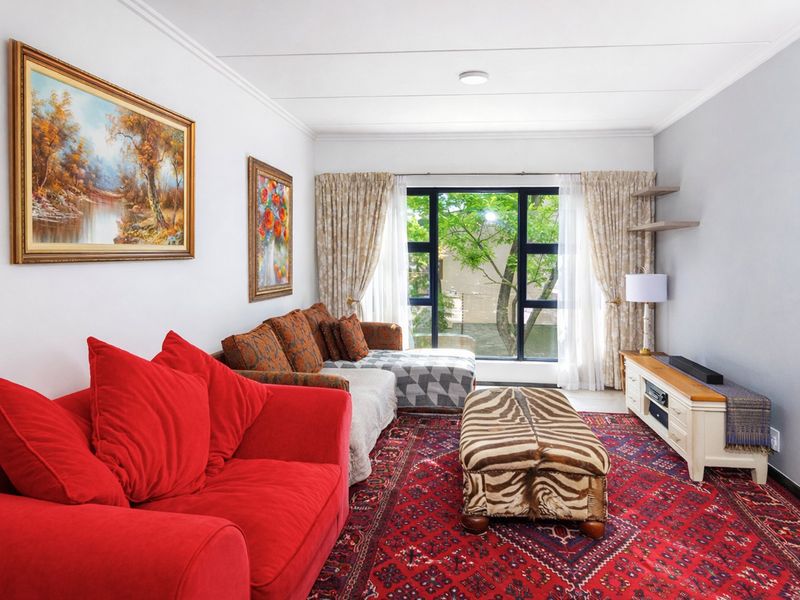 A well-lit living room featuring large windows with garden views, neutral wall finishes, and classic ceiling coving.