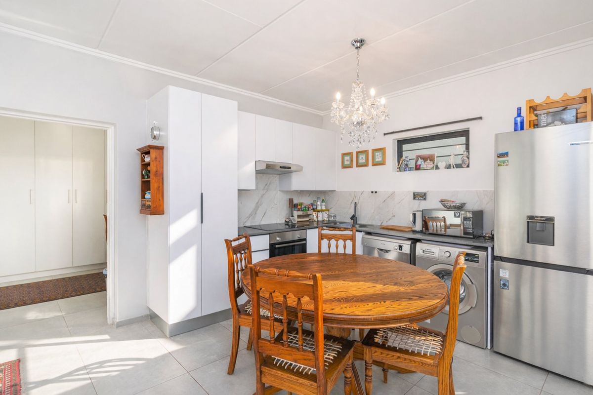 A functional kitchen featuring white cabinetry, marble-look splashbacks, integrated appliances, and tiled flooring, seamlessly integrated into an open-plan dining area.