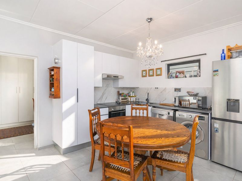 A functional kitchen featuring white cabinetry, marble-look splashbacks, integrated appliances, and tiled flooring, seamlessly integrated into an open-plan dining area.