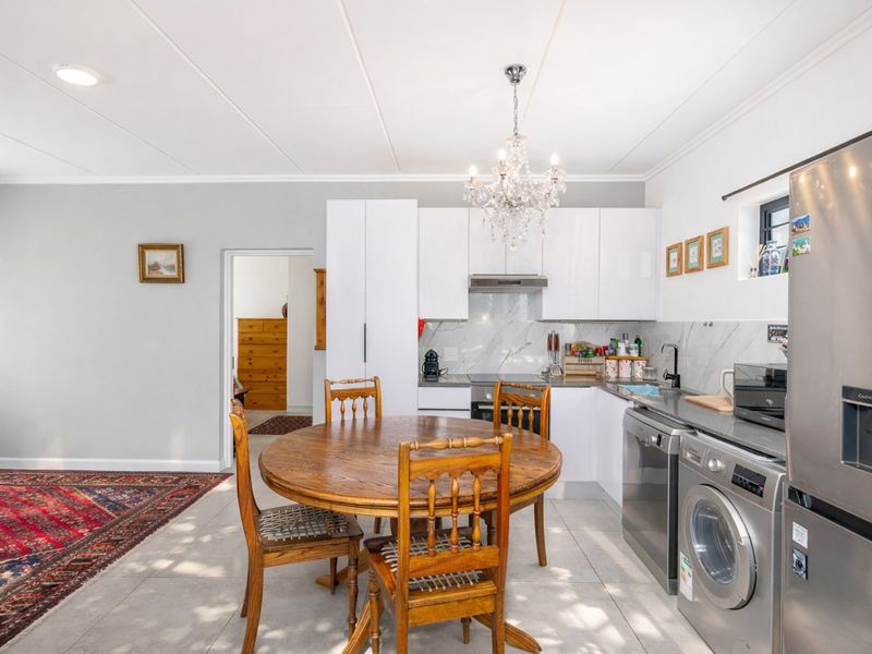 Open-plan kitchen and dining area featuring modern white gloss cabinetry, marble-look splashback, integrated appliances, and tiled flooring throughout.