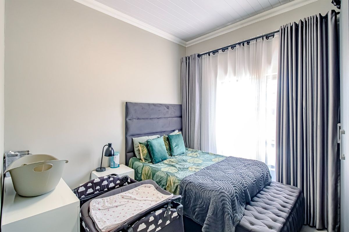 A well-maintained bedroom featuring crown molding and a tongue and groove ceiling, with large windows dressed in floor-to-ceiling curtains.