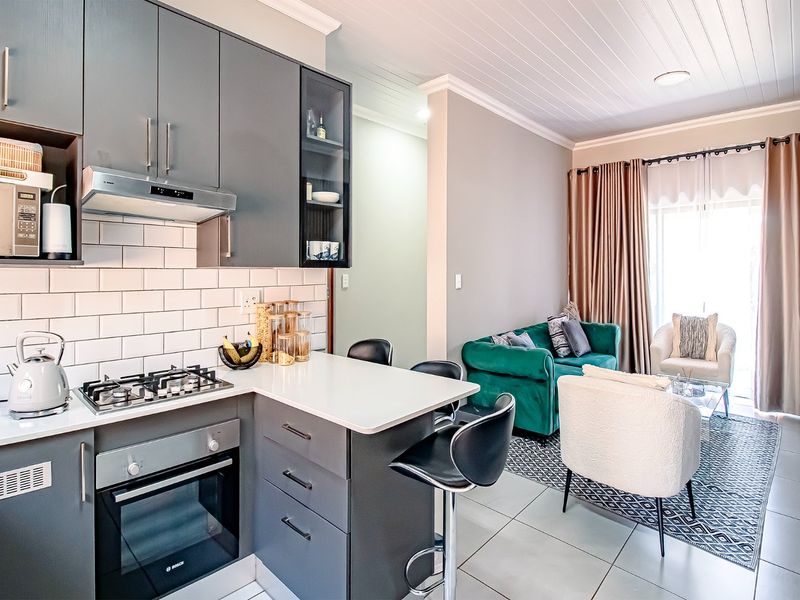 Modern open-plan kitchen and living area featuring sleek grey cabinetry, quartz countertops, subway tile backsplash, and integrated appliances, leading to a bright lounge space.