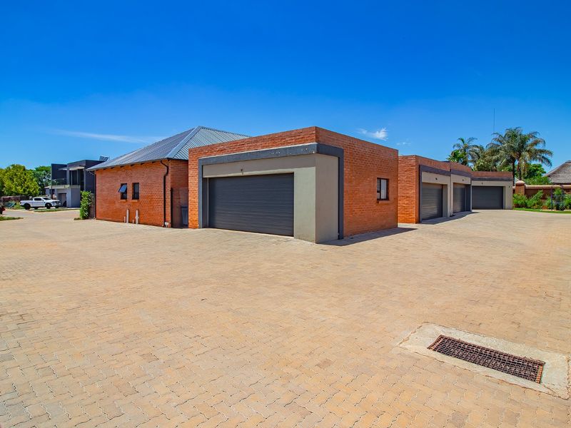 Exterior view of a townhouse complex featuring multiple garage units, a spacious paved driveway, and durable brick construction.