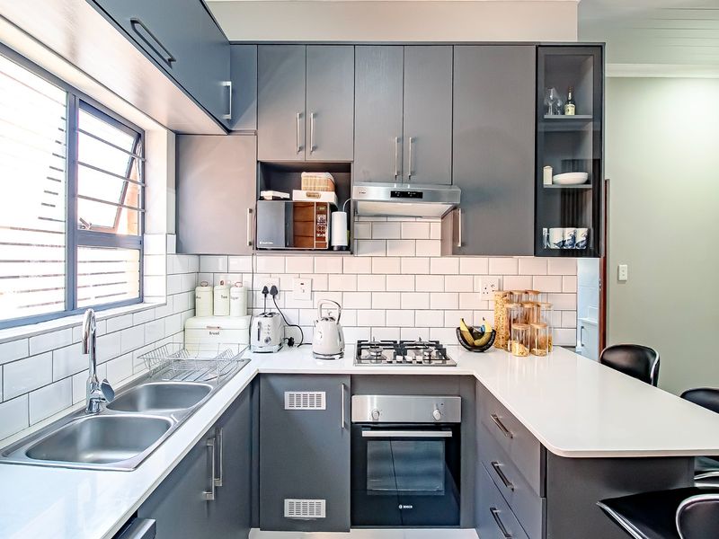 Modern kitchen featuring sleek grey cabinetry, white subway tile backsplash, quartz countertops, and integrated stainless steel appliances including a gas cooktop and oven.