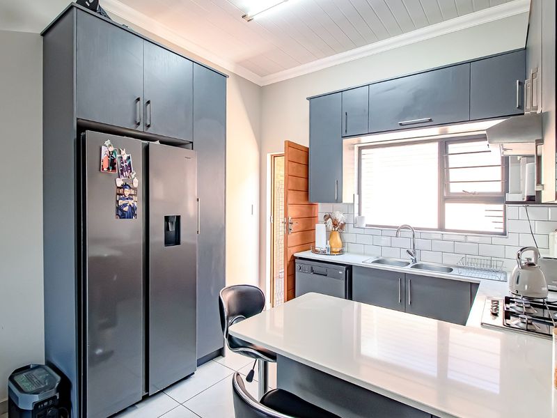 Modern kitchen featuring dark grey cabinetry, white quartz countertops, subway tile backsplash, and integrated appliances with a clean, contemporary finish.